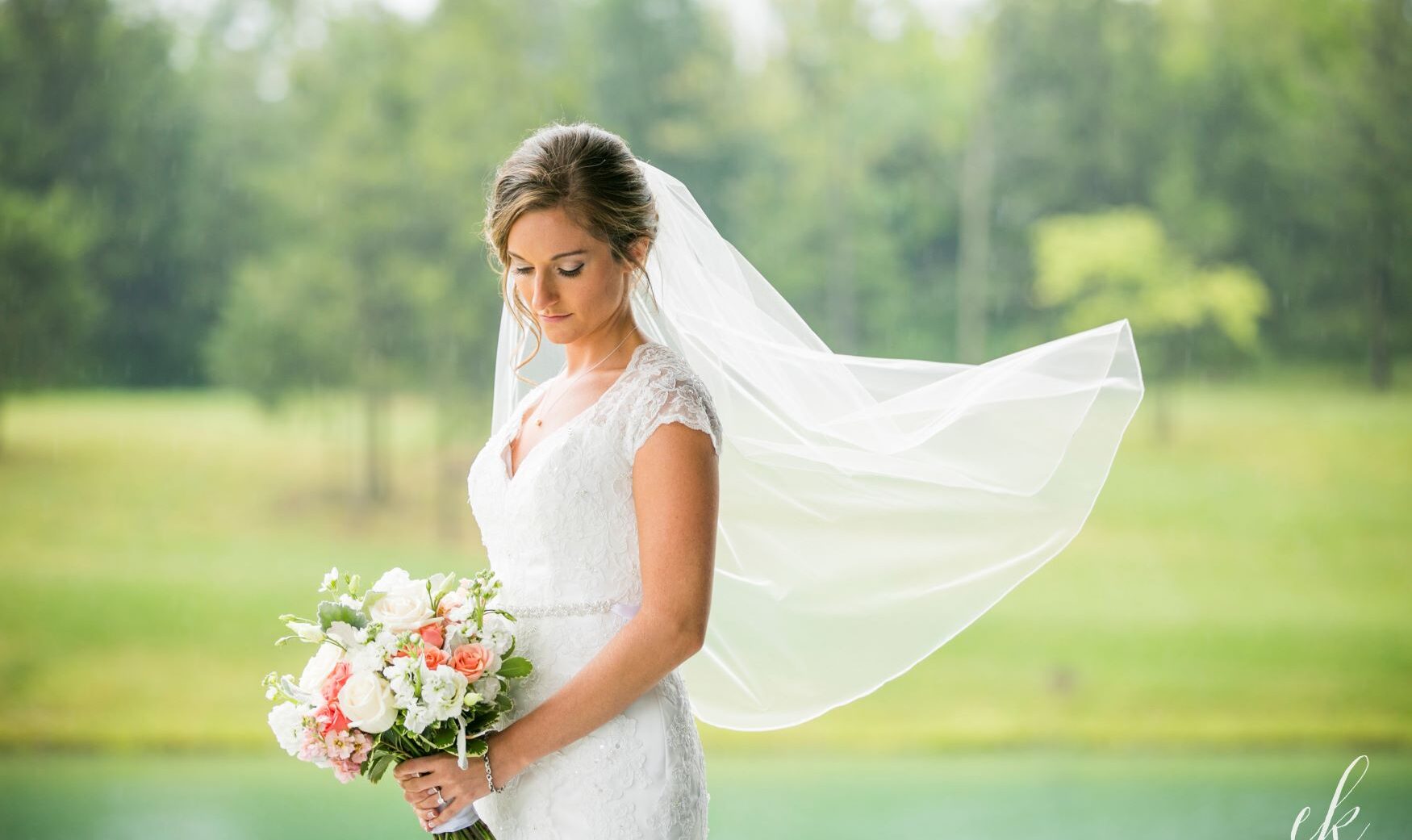 bride with veil blowing in the wind, in front of pond